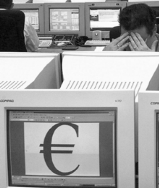 In the foreground, a Compaq computer monitor displays a large euro symbol (€) on screen. In the background, two workers are seated at desks with multiple monitors, one of whom appears to be resting their head in their hands.
