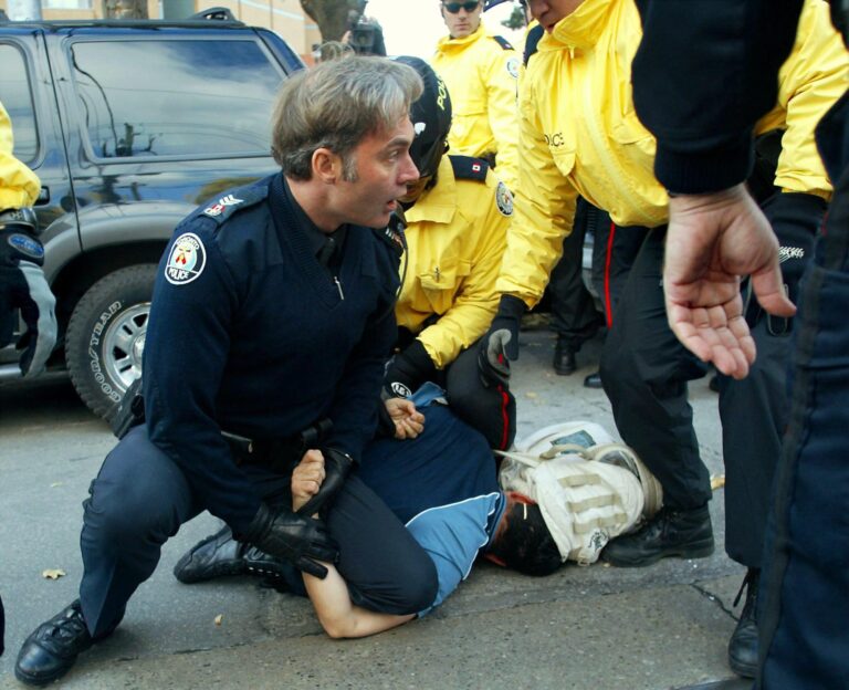 A uniformed police officer kneels on a protester.