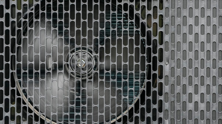 A close-up view of the grill and fan of a heat pump.