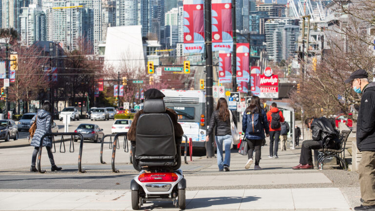 A person in a motorized wheel chair crosses a Vancouver street in March.
