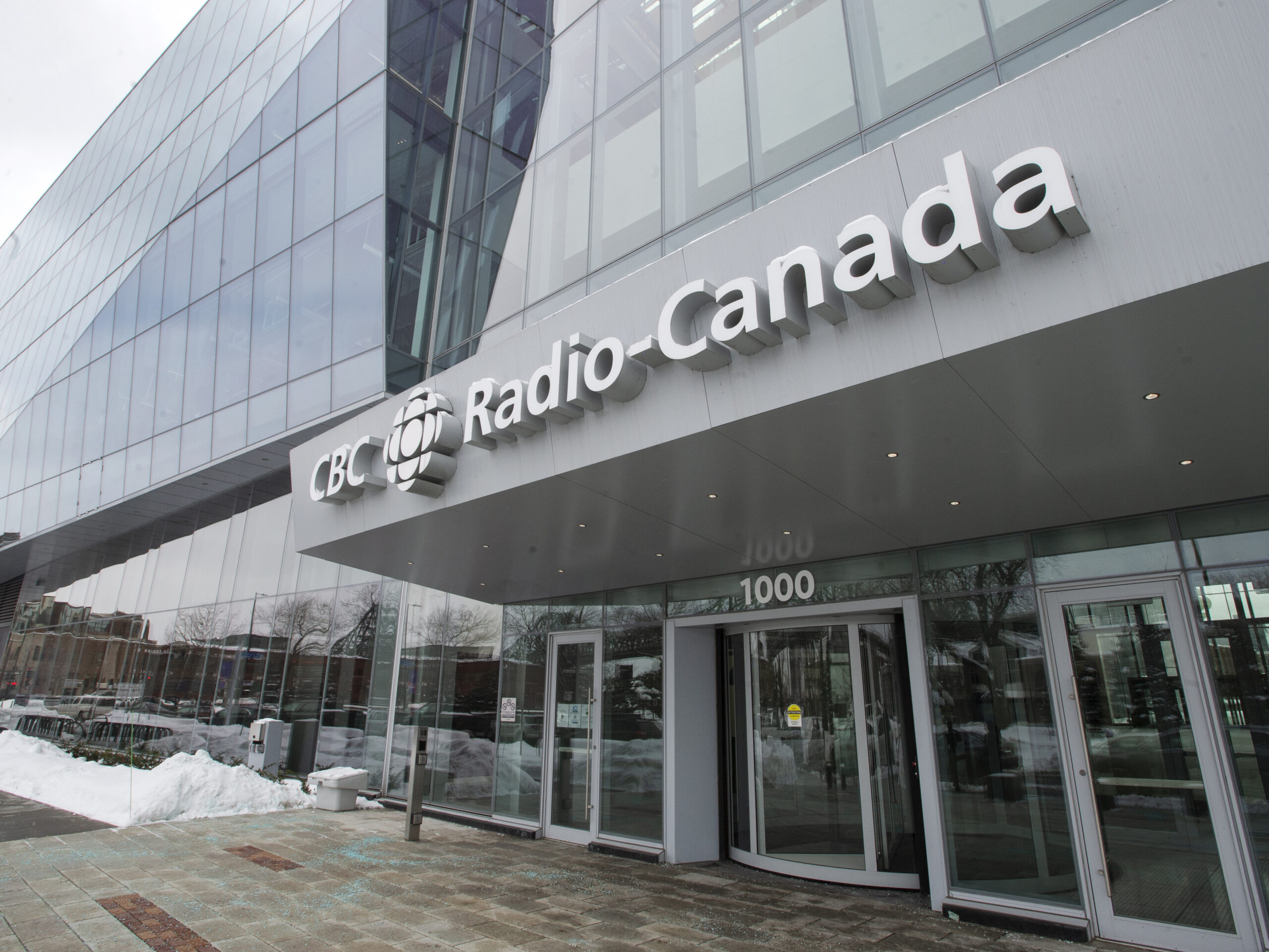 The entrance of the building has three glass doors. The building is a glass-walled modern design.