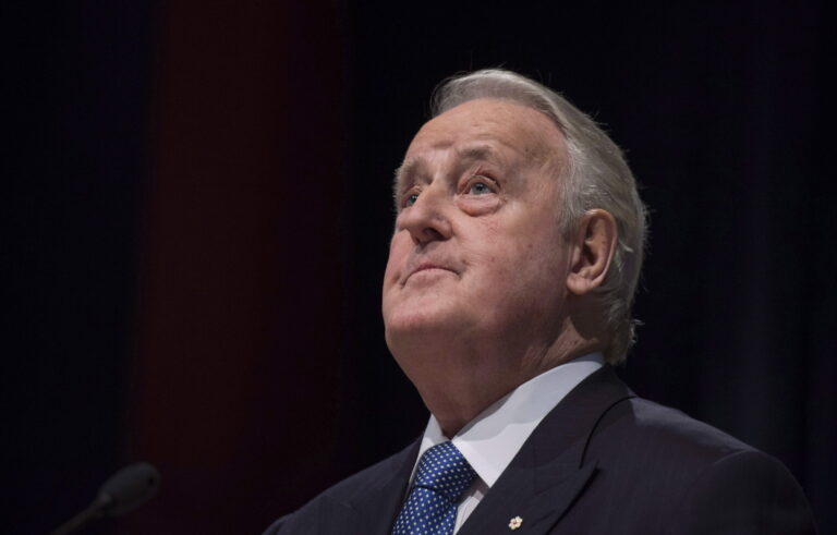 A closeup of Brian Mulroney looking skyward with a black background.