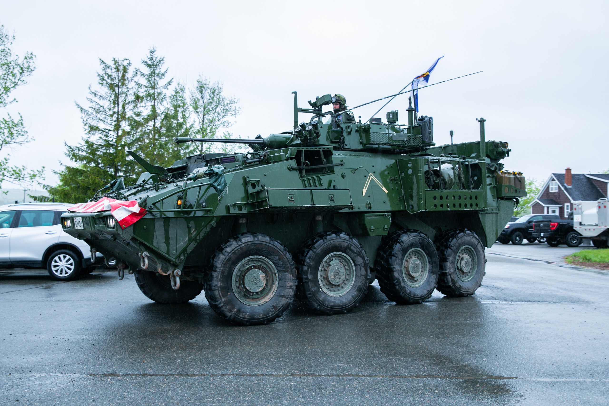 Un soldat dans un uniforme vert foncé conduit le véhicule depuis une ouverture sur le toit. Le véhicule est vert avec quatre pneus larges sur les deux côtés.