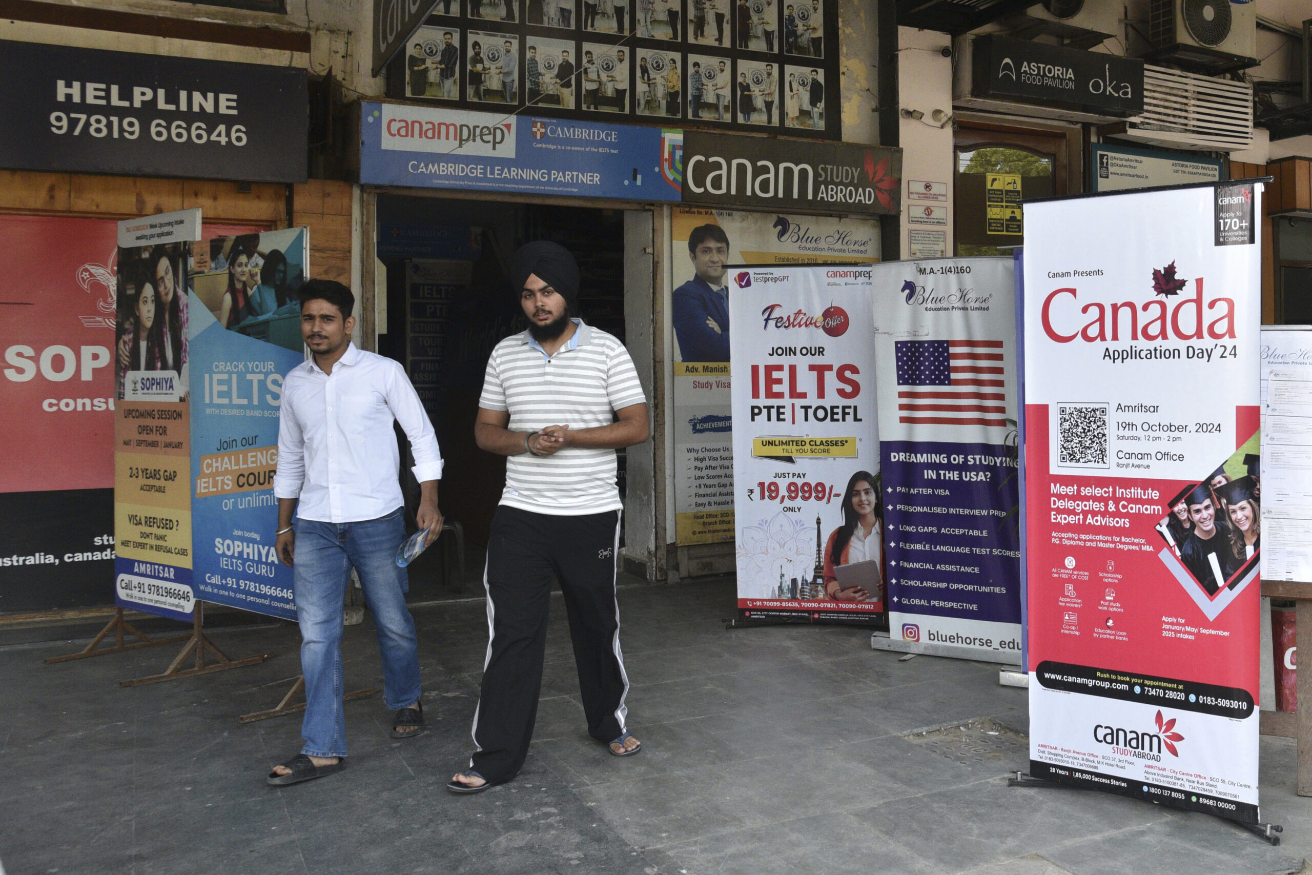 Two young men walk past five life-size posters positioned outside a building plastered with ads. Each poster advertises a study-abroad opportunity, including one for Canada.
