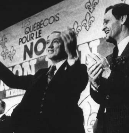 Jean Chrétien applaudit Pierre Elliot Trudeau qui salut la foule.