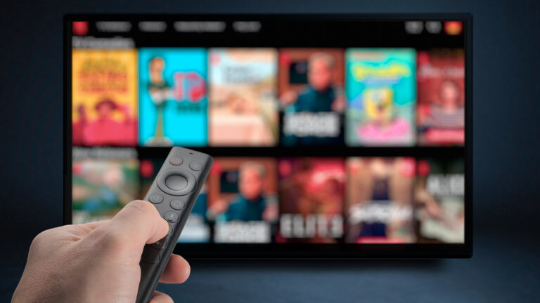 A hand with a remote control in front of a TV screen showing a menu with a myriad of choices.