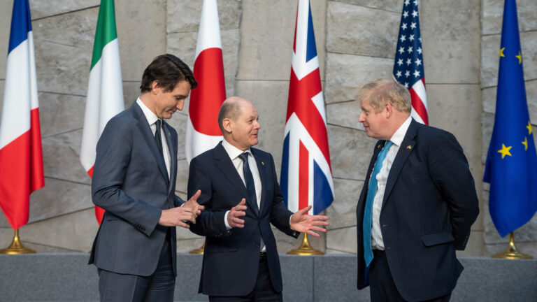 Prime Minister Justin Trudeau, left, talks with German Chancellor Olaf Scholz, center, and British Prime Minister Boris Johnson, right, in front of the flags of NATO countries.