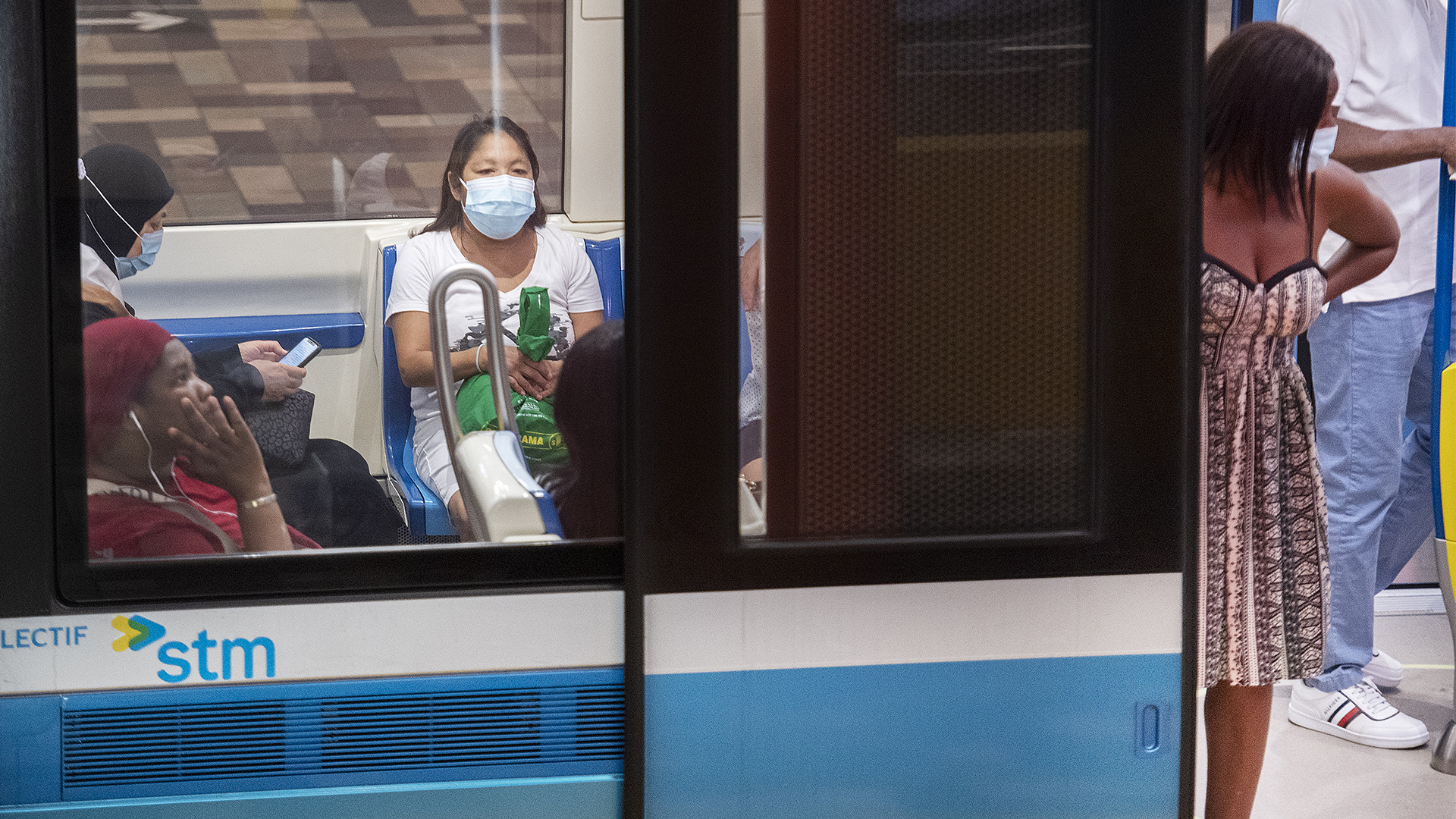People, some sitting, some standing, sport light-blue masks during a stop at a station.
