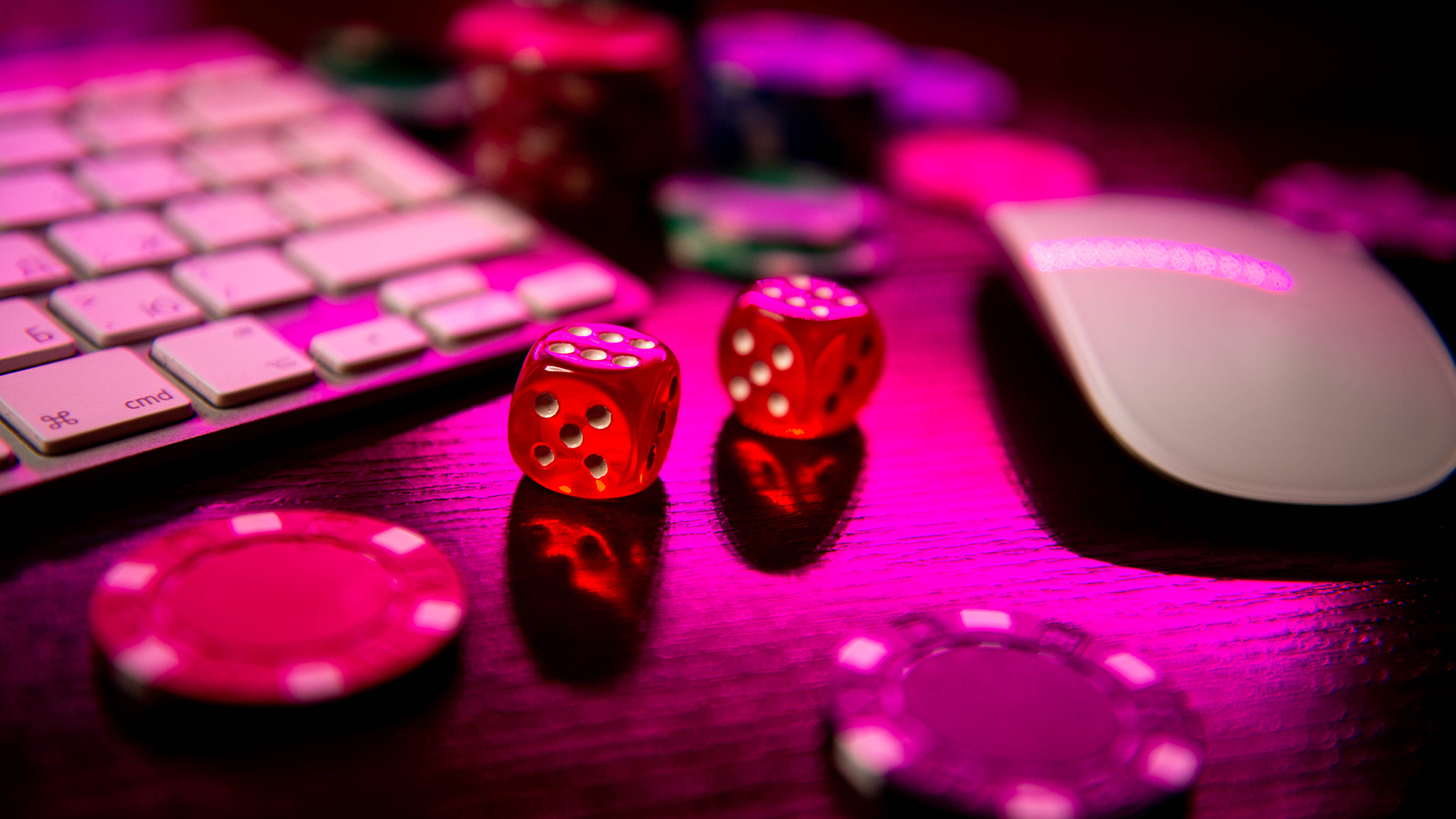 Poker chips and dice sit next to a computer keyboard and mouse under a pink light.