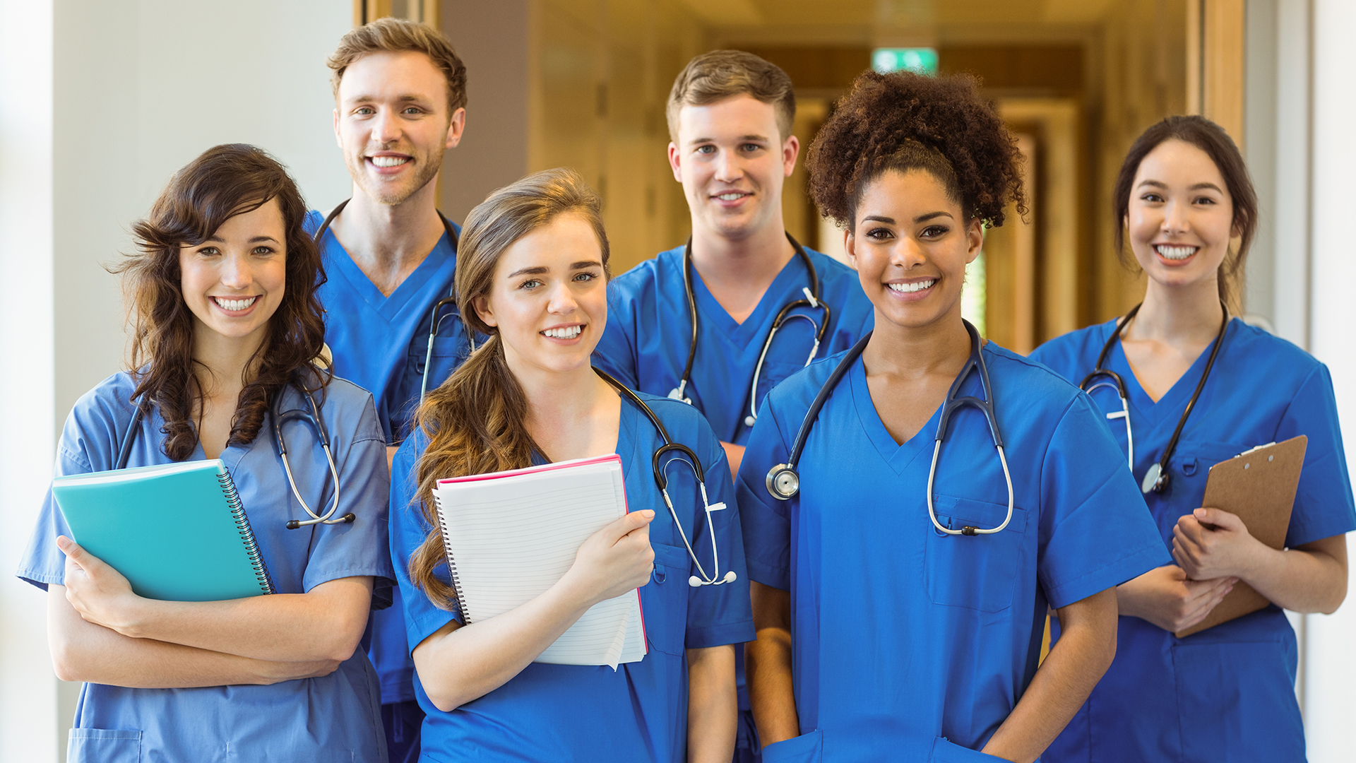 Six étudiants en médecine portant leur uniforme bleu et leur stéthoscope, deux garçons, quatre filles, sourient à la caméra.