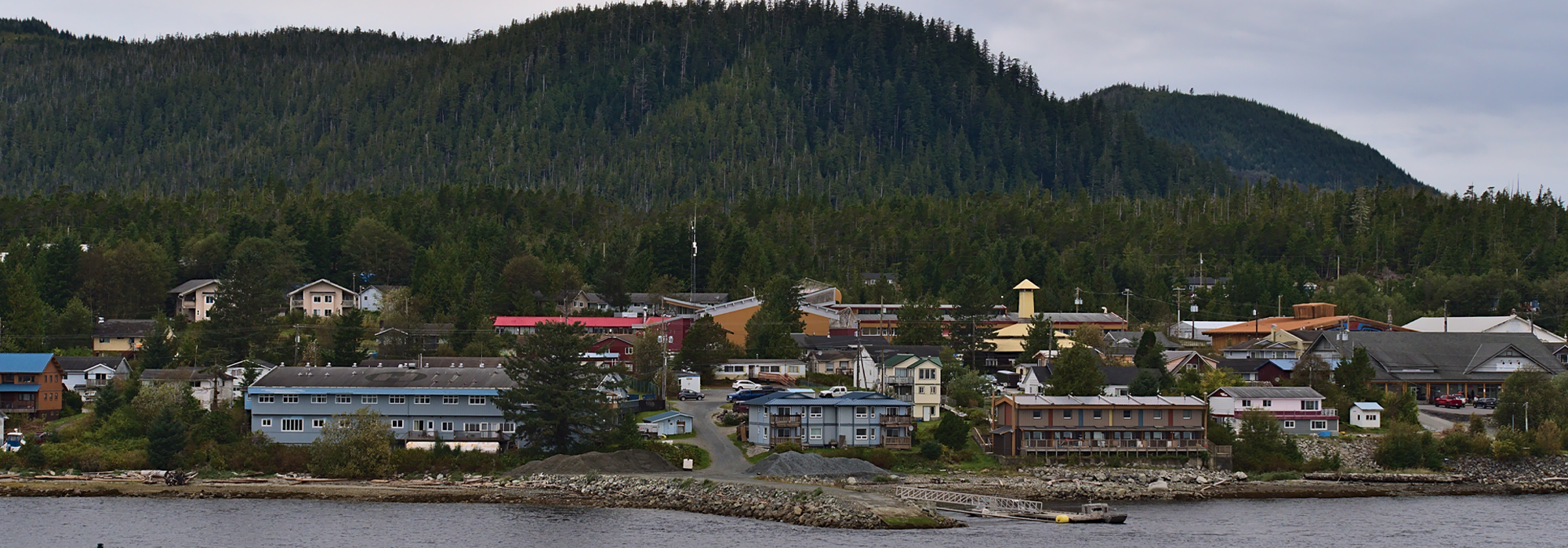A village of low-rise apartment buildings and a few shops sit between forest and the waterfront.