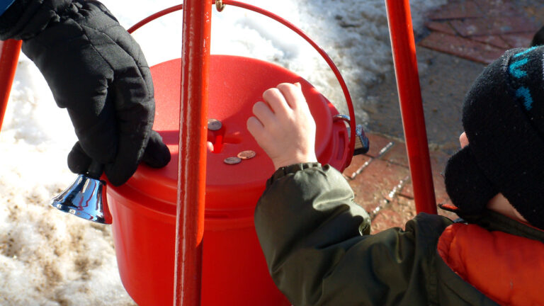 A small child puts spare change into a red donation bucket.