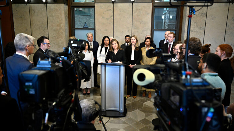 Freeland is at the podium with about a dozen people around her.
