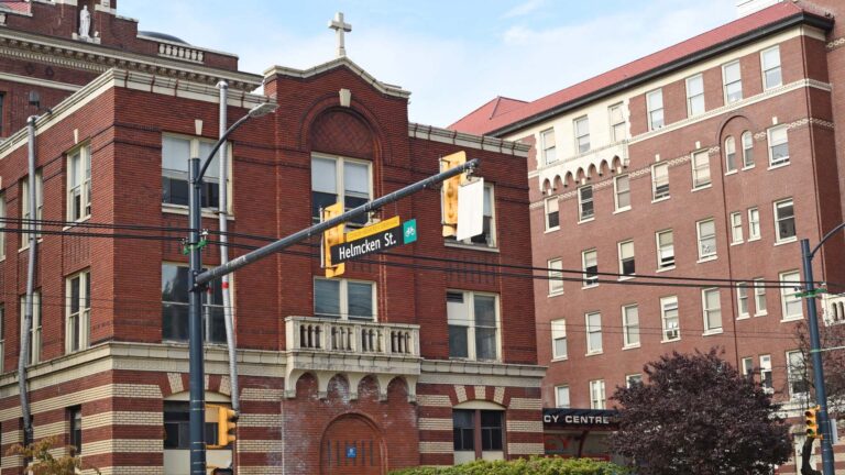 Several wings of the brick building are lined with evergreen hedges and small trees. At the top of one three-storey building, a white cross lets people know the hospital is faith-based.