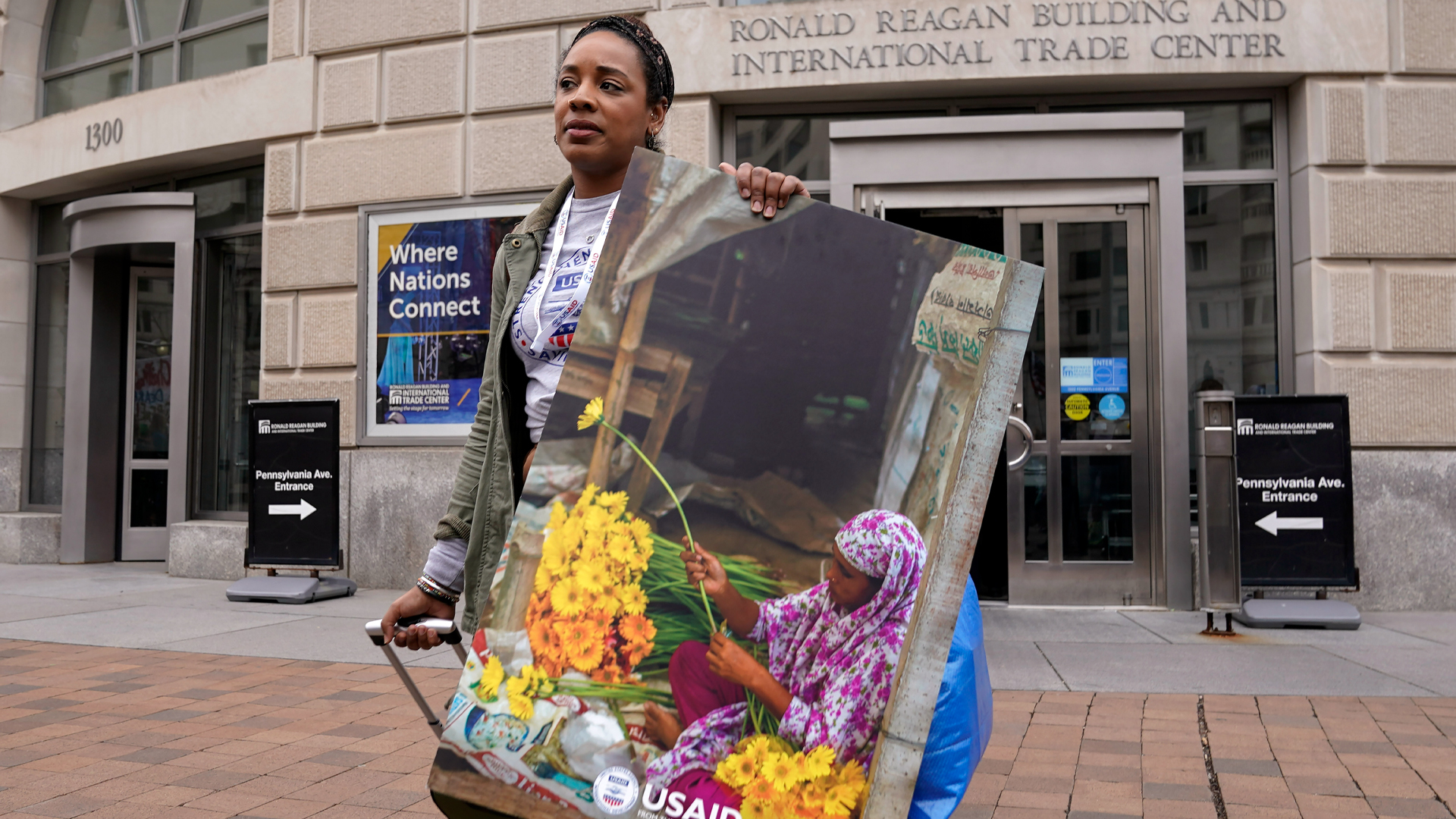 A woman carrying a USAID poster featuring a woman cutting flowers walks out of her office with her belongings.