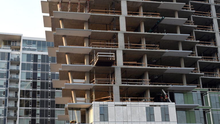 Ten storeys of a condo tower are visible, with a finished 10-storey building behind it. The floors of the building under construction are without walls and windows. The upper floors extend out farther than the lower floors, creating a subtle v-shape for the building.