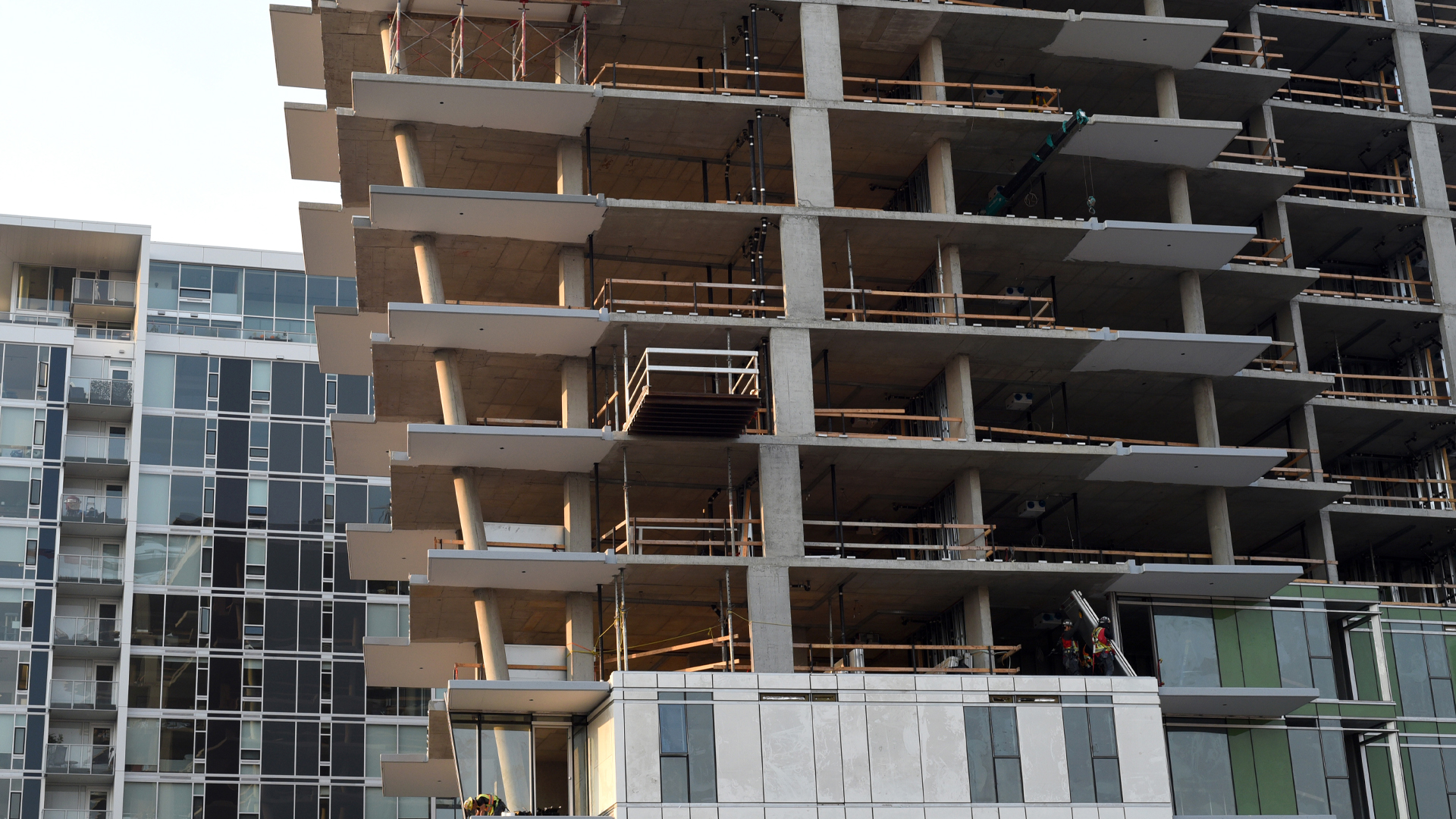 Ten storeys of a condo tower are visible, with a finished 10-storey building behind it. The floors of the building under construction are without walls and windows. The upper floors extend out farther than the lower floors, creating a subtle v-shape for the building.