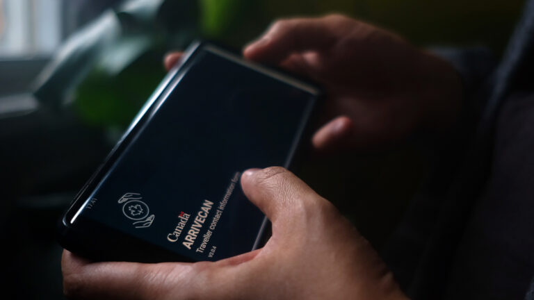 Two hands holding an electronic device with the opening screen of the ArriveCAN app.