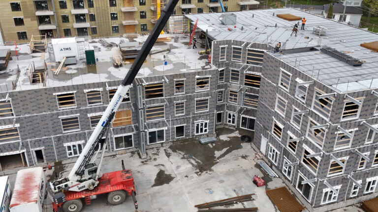 Two low-rise buildings are underway next to each other, with a handful of workers on the roof of one and a crane hovering over-head.