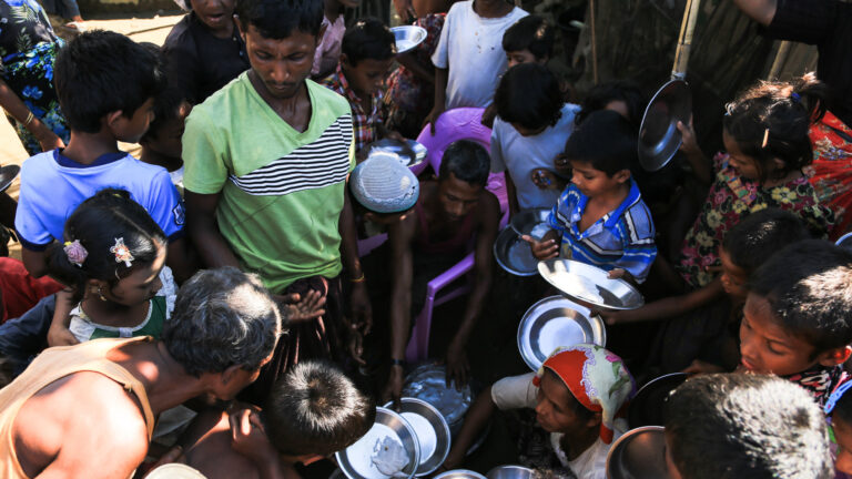 A couple dozen people young and old gather around holding metal plates.