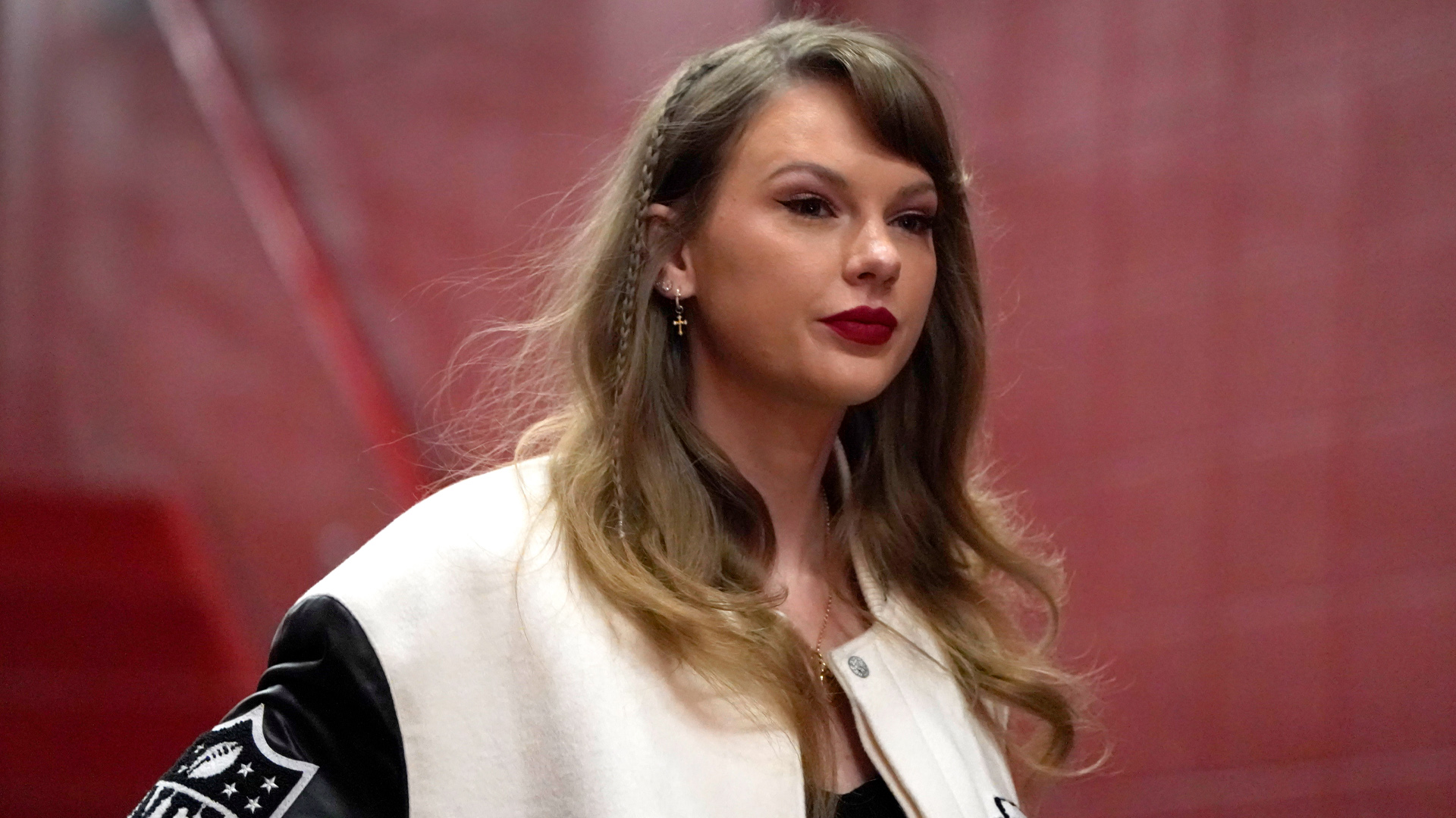Taylor Swift wearing a white coat with black sleaves and an NFL logo on the sleeve.