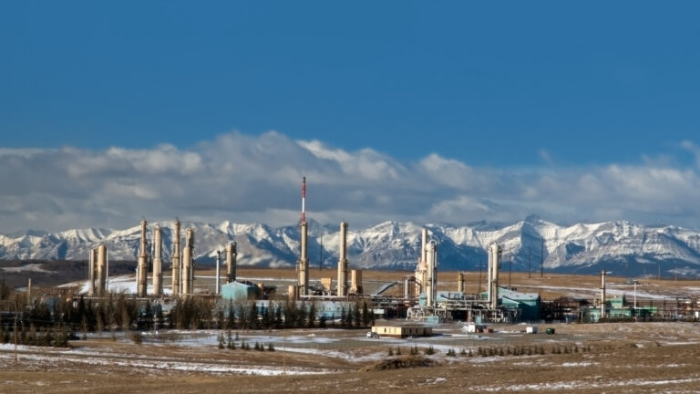 A gas plant near Cochrane Alberta is pictured in front of a snow-capped mountain range.
