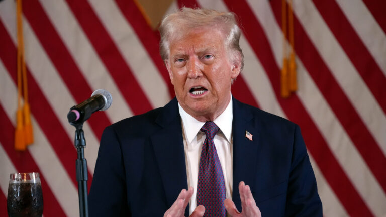 Donald Trump speaking in front of an American flag.