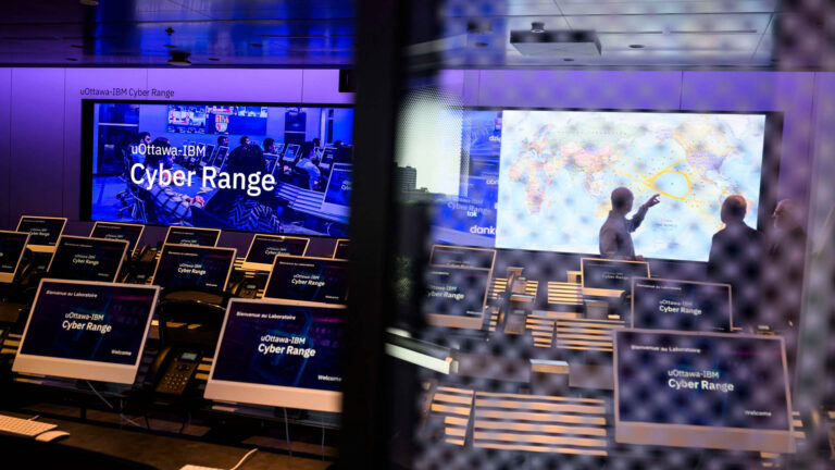A series of computers are lined up in command-centre style with a map of the world in front of the room. The image is partially obscured by a screen, providing an element of intrigue.