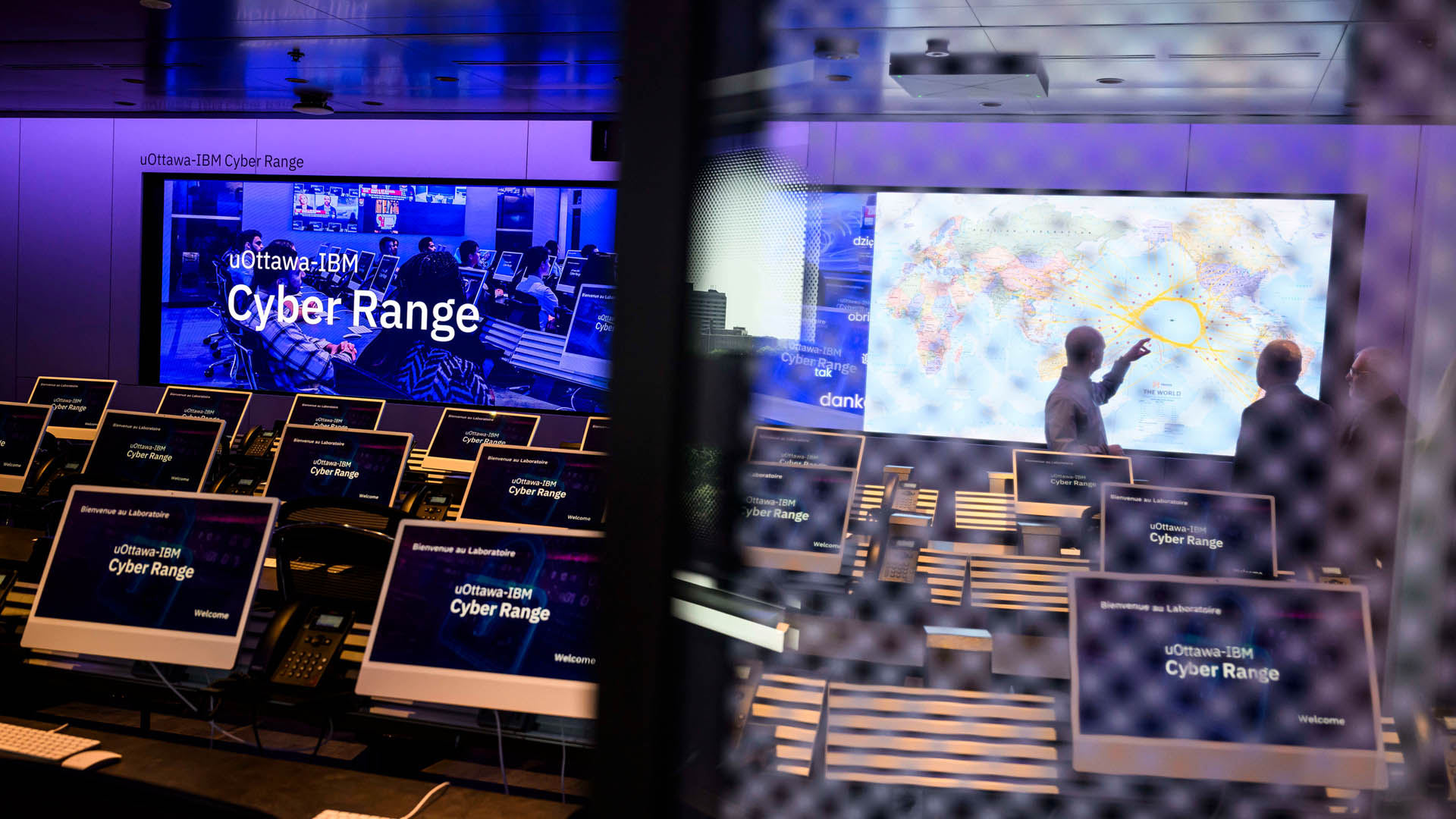 A series of computers are lined up in command-centre style with a map of the world in front of the room. The image is partially obscured by a screen, providing an element of intrigue.