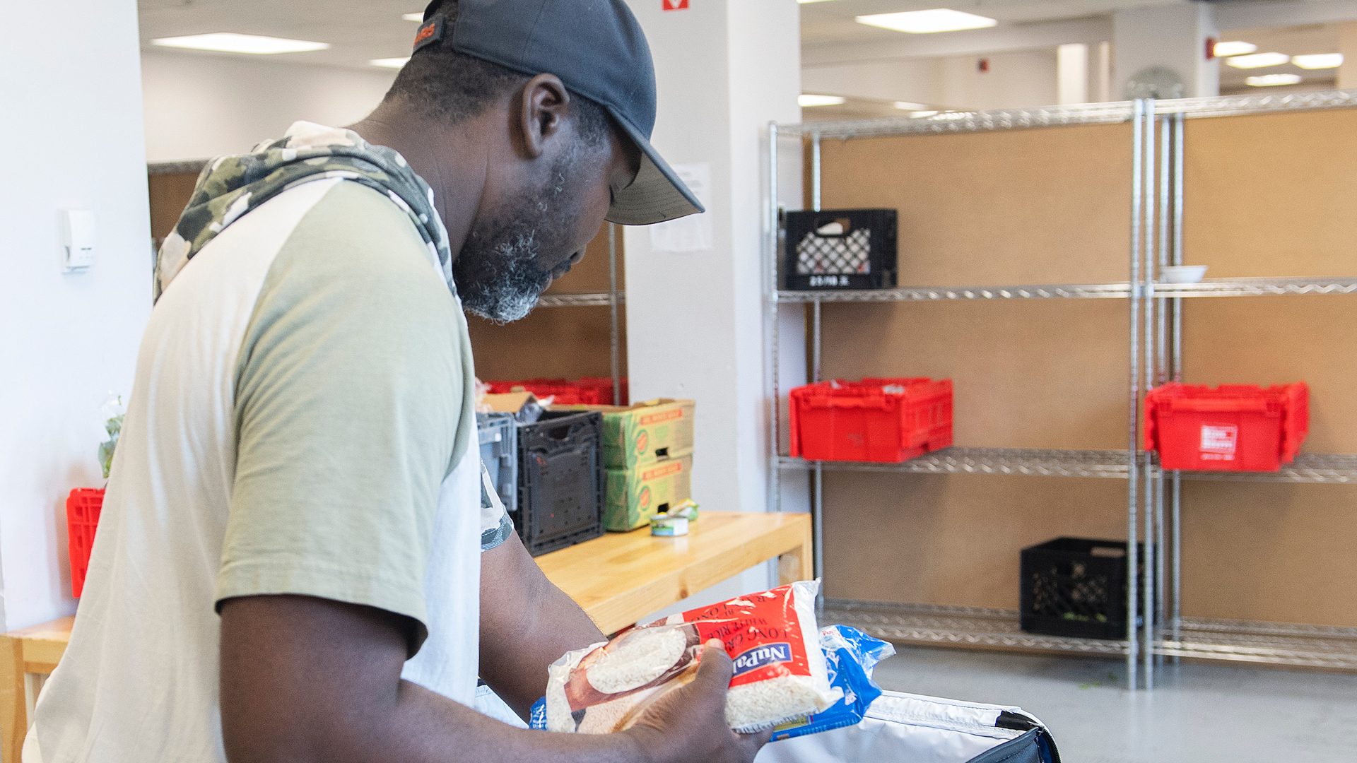 A man places a bag of rice into an insulated bag, with mostly empty shelves in the background.