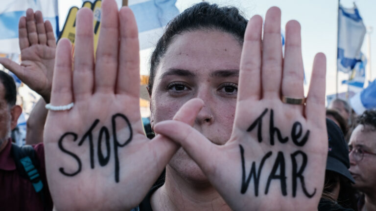 A woman holds up her hands with a message reading “Stop the war” written in black ink in her palms.