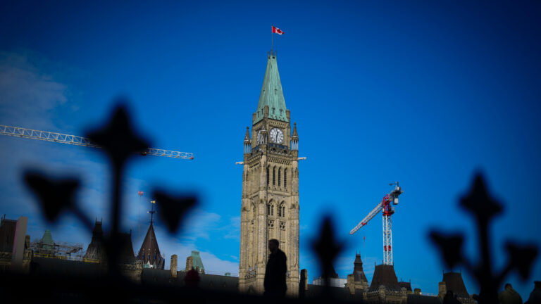 Parliament’s peace tower is seen through the shadows of a wrought-iron fence.