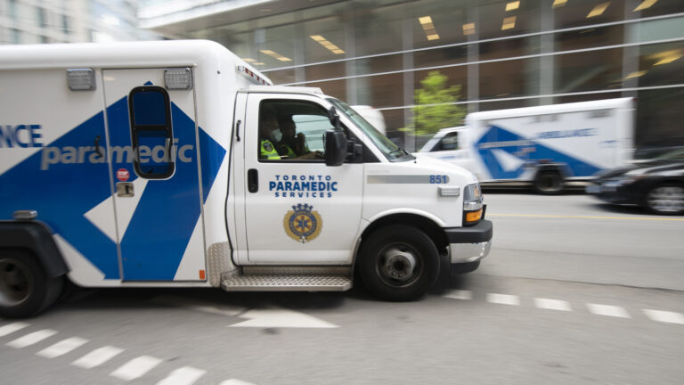 Le véhicule est blanc avec un marquage bleu. Le photographe a suivi l’ambulance en mouvement alors qu’elle passait devant un bâtiment vitré situé de l’autre côté de la rue, et qui est flou sur l’image.
