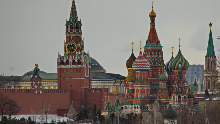Colourful, elegant spires of the Kremlin surrounded by snow covered ground, cloudy sky and trees.