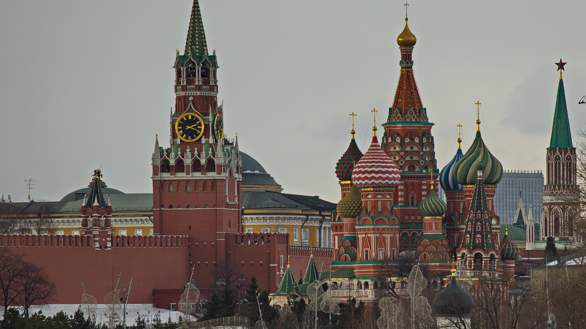 Colourful, elegant spires of the Kremlin surrounded by snow covered ground, cloudy sky and trees.