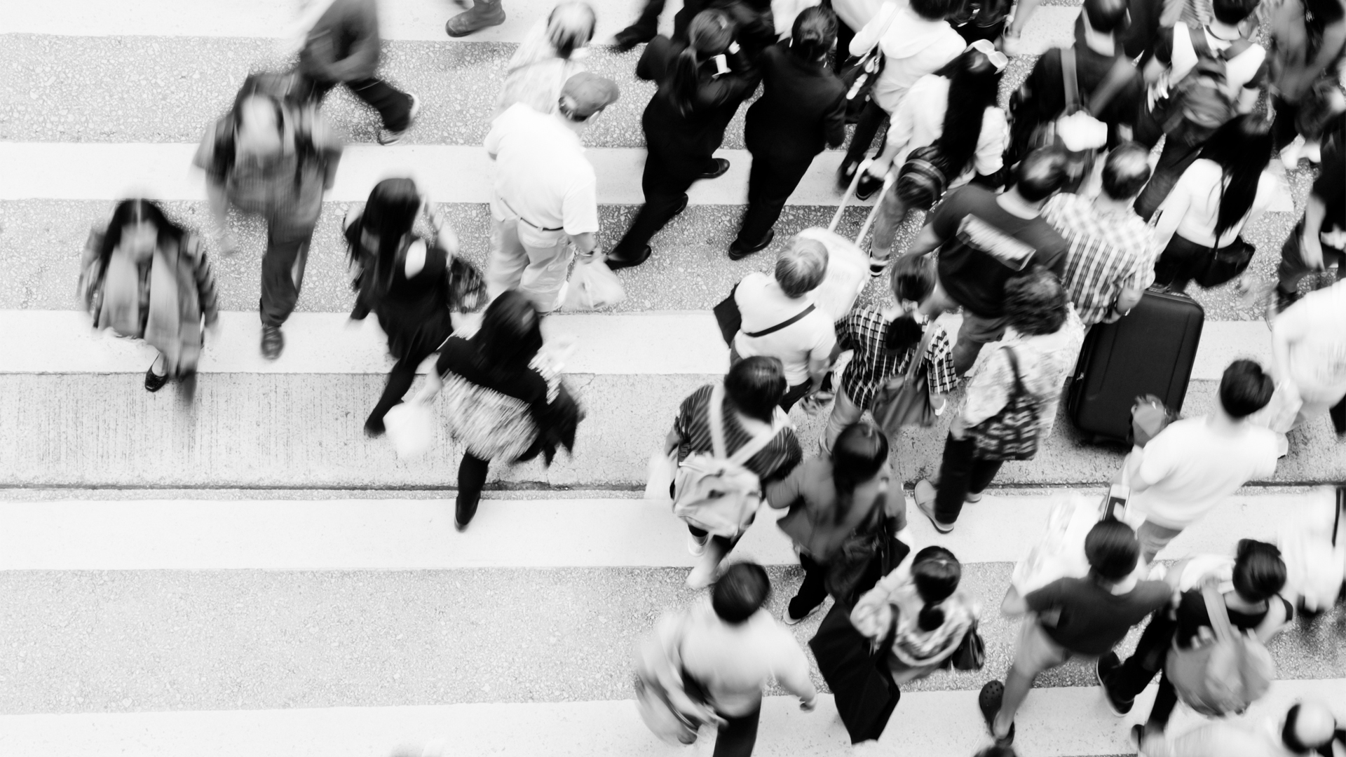 A black and white overhead image of a crowd moving through a crosswalk.