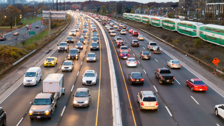 A photo of traffic on a three-lane highway with a train running alongside.