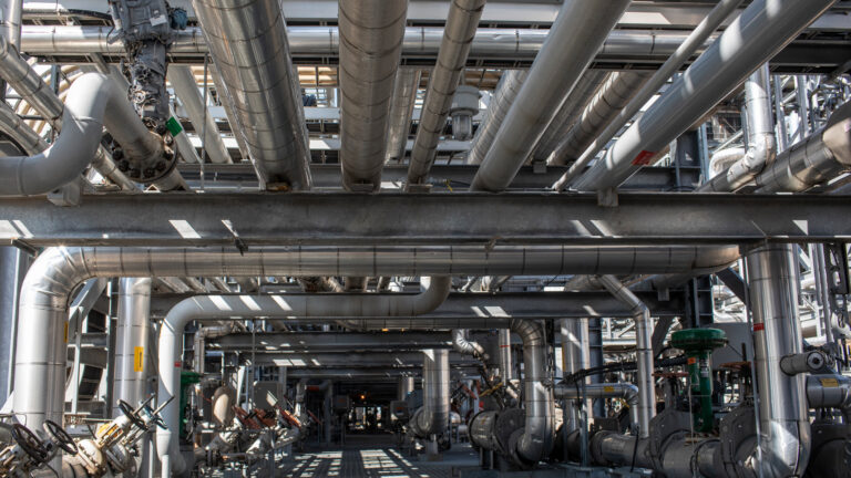 Metal tubes and vents and steel supports form a structure several storeys high, with sunlight streaming in through the gaps.