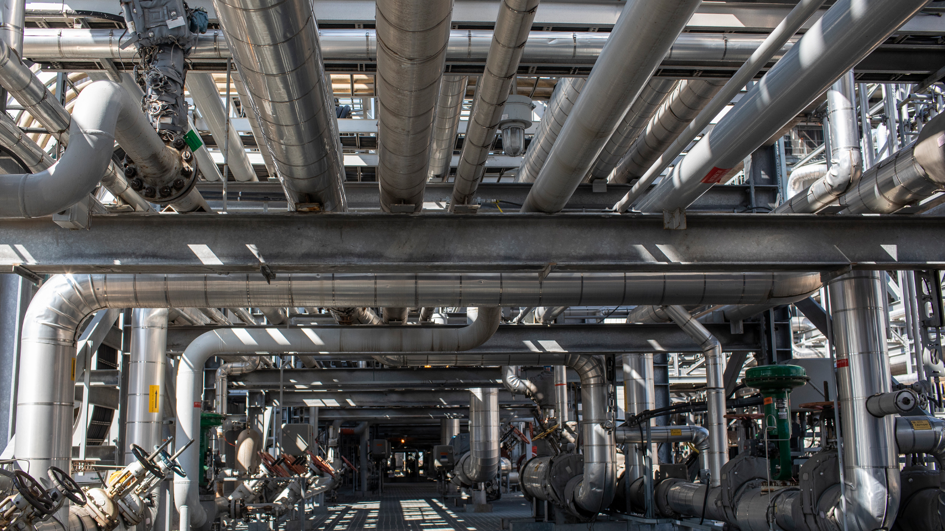 Metal tubes and vents and steel supports form a structure several storeys high, with sunlight streaming in through the gaps.
