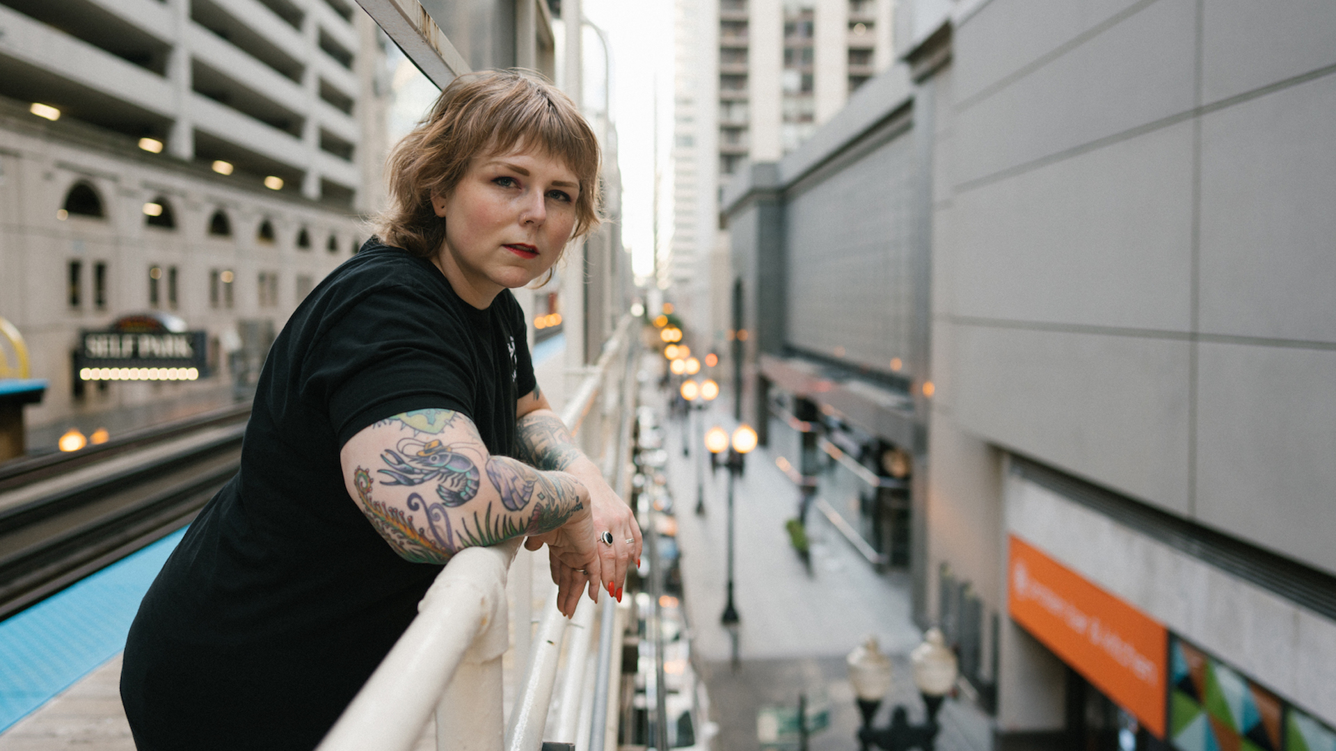 The author leans against a railing on a railway platform over a nondescript city street near a parking garage.