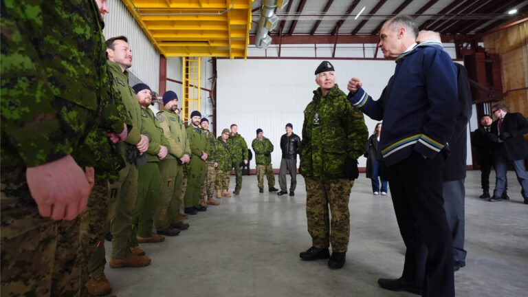 Mark Carney is wearing a blue traditional Inuit pullover called the atigi while speaking to soldiers wearing their green uniforms.
