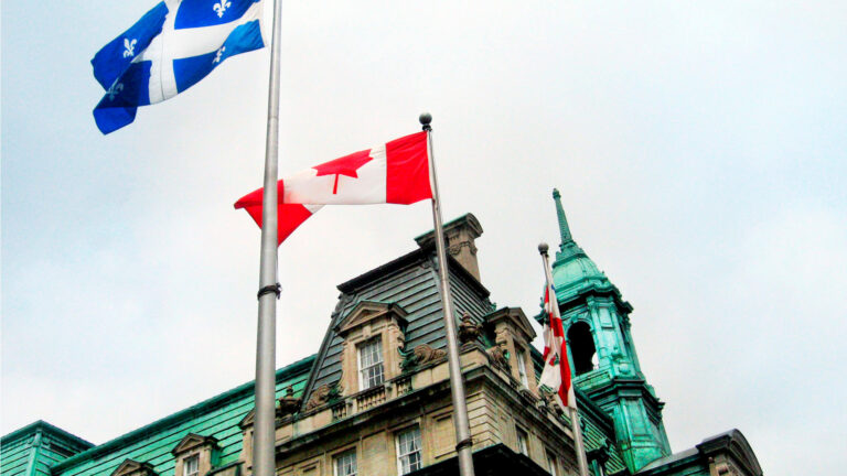 Montreal City Hall, close-up view from below, with the flags of Canada and Quebec flying in the foreground.