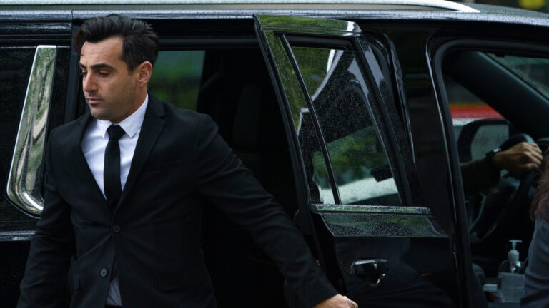 Hoggard is stepping out of a black SUV. He is in a black suit with black tie and white shirt. 