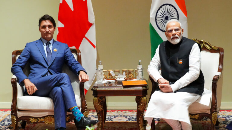 The two prime ministers sit in armchairs with their respective flags behind them.
