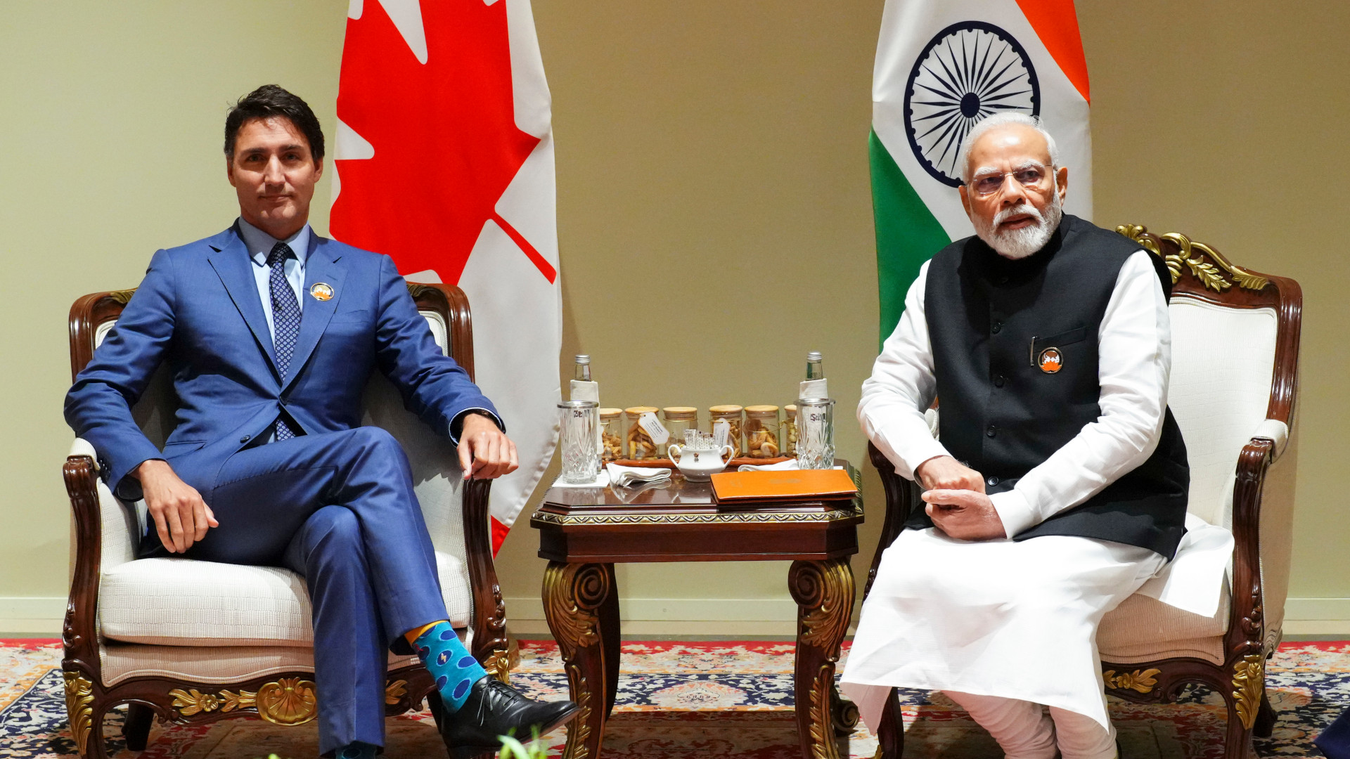 The two prime ministers sit in armchairs with their respective flags behind them.