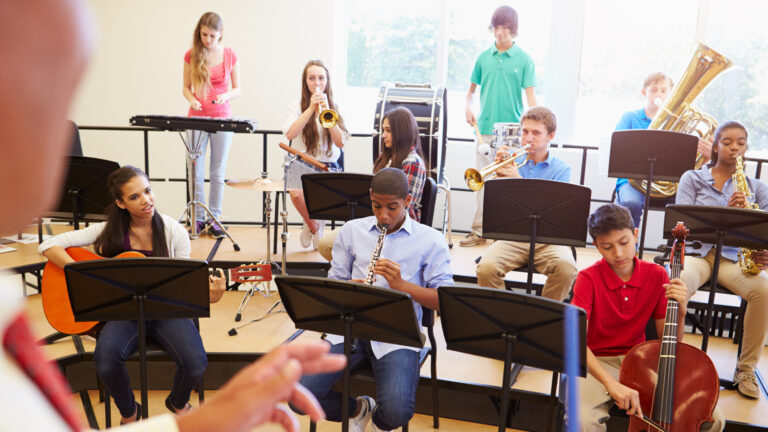 A stock photo showing 10 children playing musical instruments in a classroom.