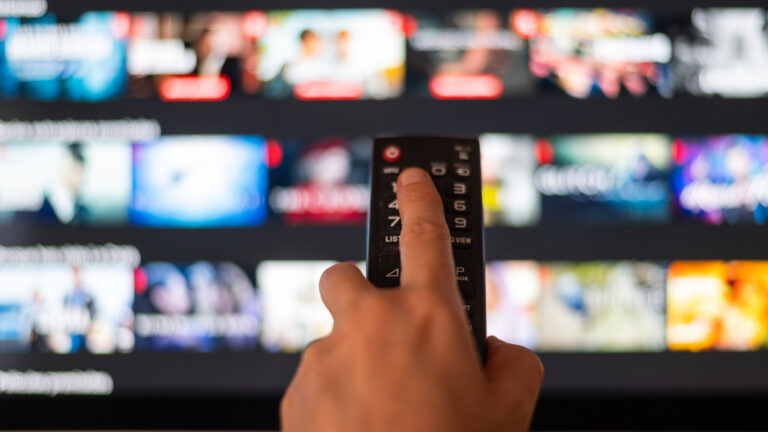 A hand holding a remote control in front of a television.