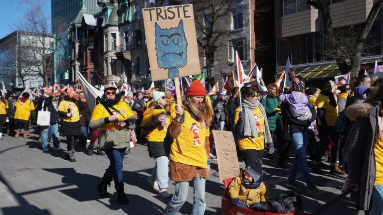 Des femmes vêtues de dossards jaunes manifestent dans une rue de Montréal en soulevant des pancartes.