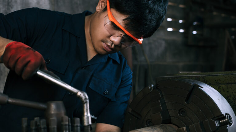 An Asian man is doing mechanical work in a factory. He is wearing safety glasses.