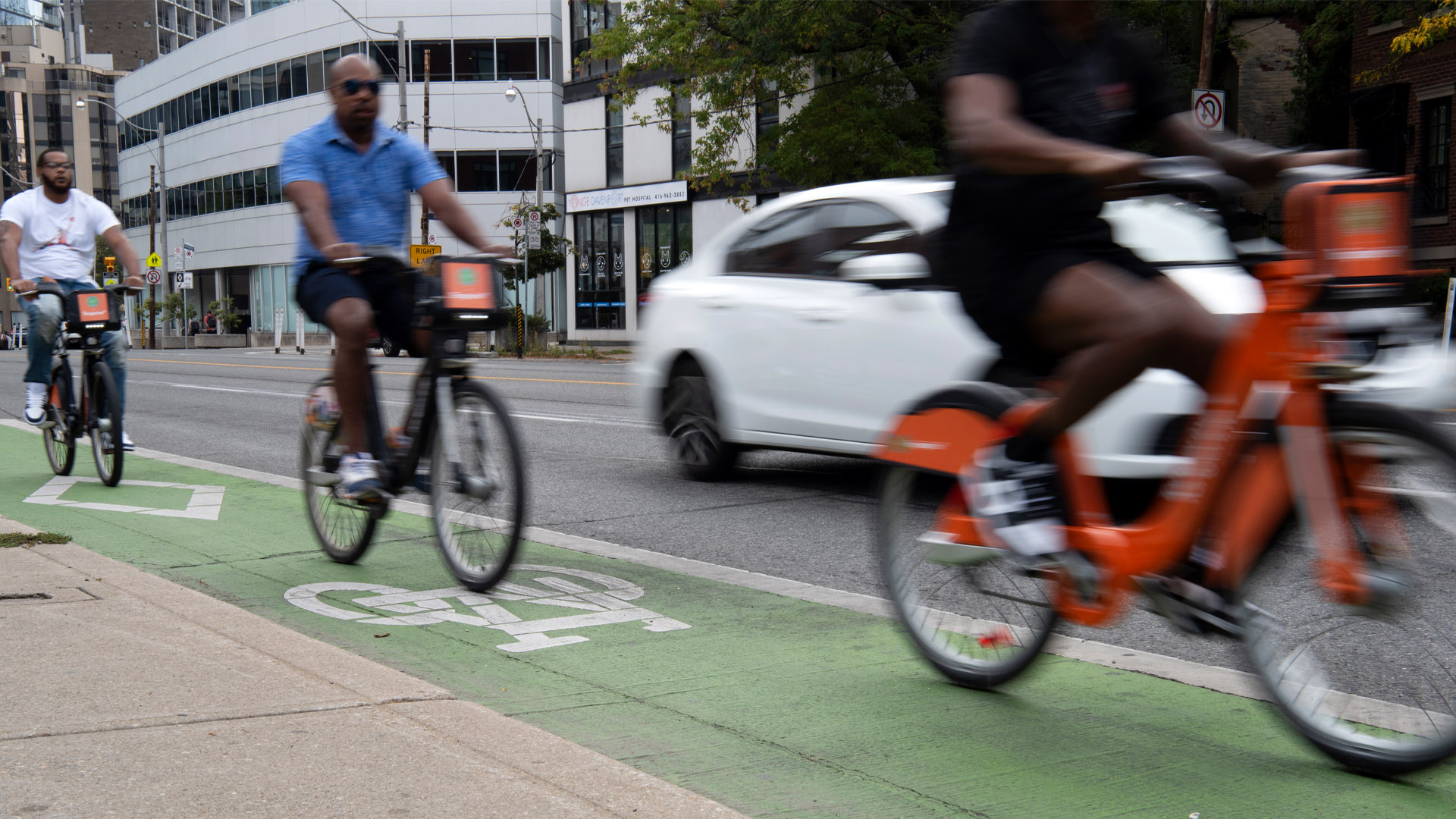 Three cyclists use the lane, which is painted in fading green. A white car passes them.